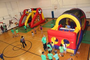Children on the far right climb inside an inflatable obstacle challenge course while children on the left play “Soccer Fever” on an inflatable game in the gym at Vacation Bible School on July 30, 2015.